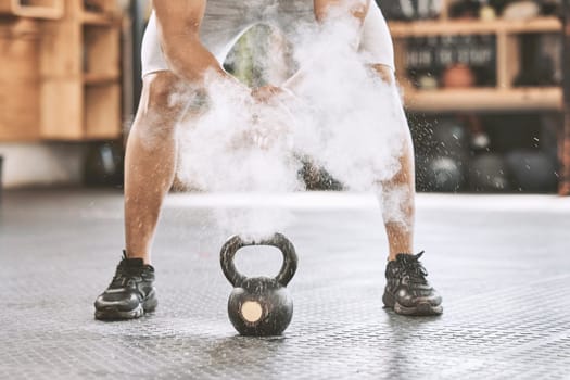 Dusting before power lifting. Bodybuilder getting ready to lift a heavy kettlebell. Athlete ready to lift weights. Sporty, muscular trainer using powder before a weight lifting routine.