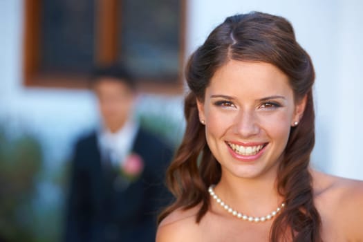 Marriage suits her. Portrait of a blushing bride smiling at the camera with her new husband in the background.