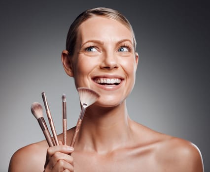 Beautiful mature woman posing with makeup brush in studio against a grey background