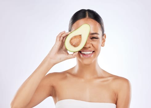 Foods high in fat are fantastic for skin. a young woman covering her eye with an avocado against a studio background.