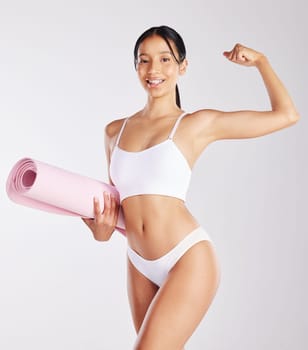 This body is thanks to yoga and a little cardio. a fit young woman holding a yoga mat while standing against a studio background