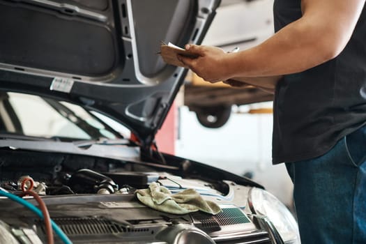 Regular auto maintenance can prevent unexpected breakdowns and accidents. a mechanic holding a clipboard while working in an auto repair shop.