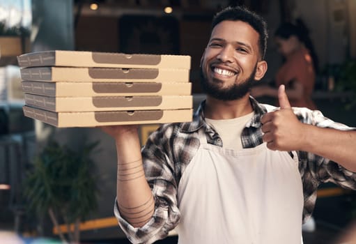 Weve got the best pizza in the city. a handsome young man standing outside his restaurant and holding a stack of pizza boxes.