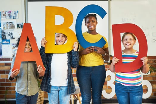 Colour helps children learn better. a diverse group of children standing and holding the alphabet letters in their classroom at school.