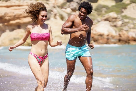 Happy black man sprinting with girlfriend in seawater