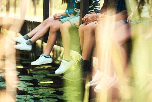 Nature knows how to get kids to relax. a group of unrecognisable teenagers sitting on a bridge in nature at summer camp.