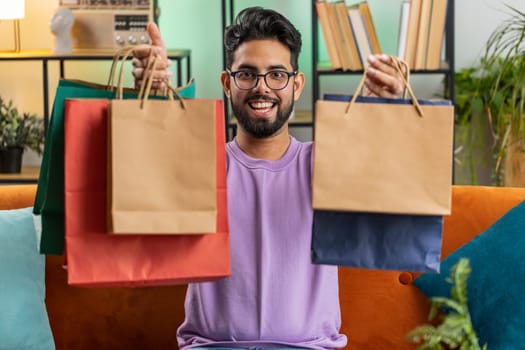 Happy indian man shopaholic consumer came back home after online shopping sale with bags at home