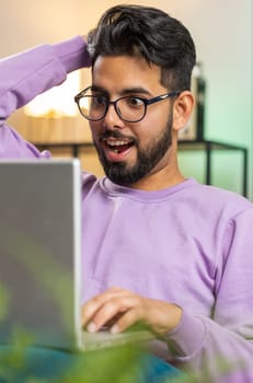 Amazed indian man use laptop computer, receive good news message, shocked by victory, celebrate win