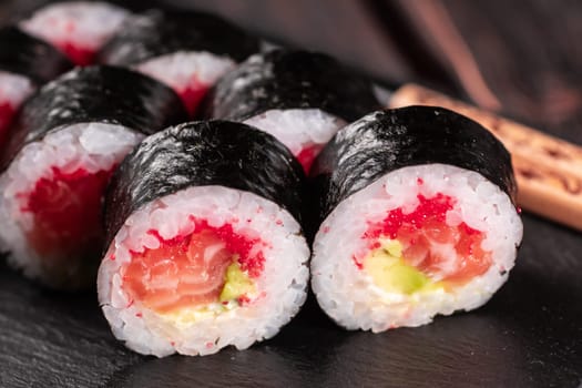 Maki sushi roll with salmon avocado and tobiko caviar served on black board close-up - Japanese food