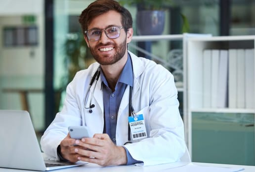 Doctor, desk and phone with smile for texting, communication or chatting and good connection at hospital. Happy man healthcare or medical professional smiling for telecommunication service at clinic.