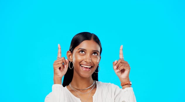 Mockup, face and Indian woman pointing up, promotion and success on a blue studio background. Portrait, female and lady with gesture for motivation, inspiration and carefree with decision and choice