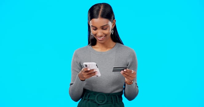 Online shopping, phone or girl with credit card in studio for payment via internet website or fintech. Happy smile, blue background or Indian woman typing money transfer via digital mobile banking