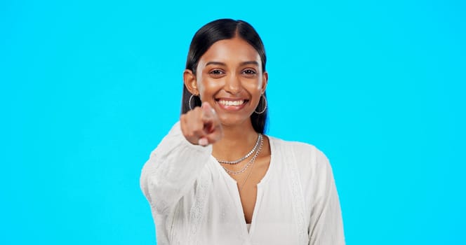Face, motivation and Indian woman pointing to you, promotion and happiness against a blue studio background. Portrait, female and lady with inspiration, choice and decision with selection and choice