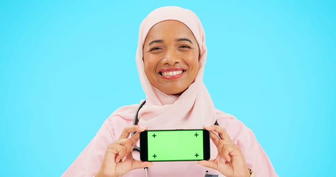 Phone, green screen and woman doctor isolated on blue background healthcare, tracking marker and mockup space. Face of nurse or muslim person with medical mobile app for advertising video in studio