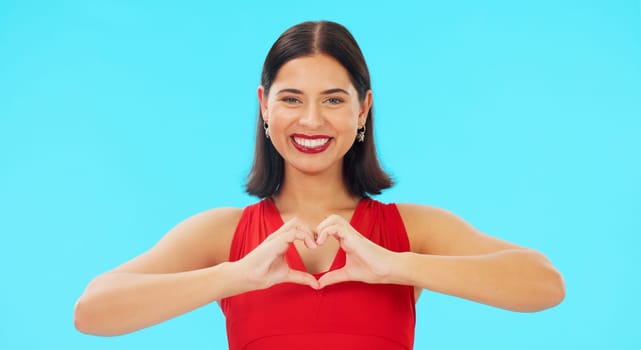 Face, heart and hands of happy woman on blue background, studio and color backdrop. Portrait, female model and finger shape of love, support and kindness for care, thanks and emoji icon, sign or hope.