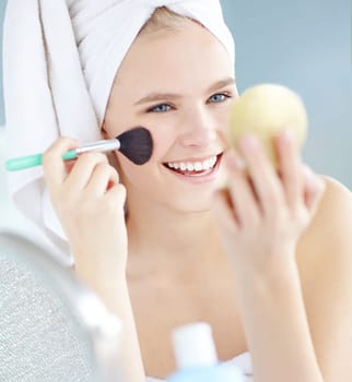 Giving her face that healthy glow. a beautiful woman applying blush with a blush brush in her towel.