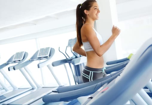 Looking and feeling great. A beautiful young woman exercising on a treadmill at the gym.