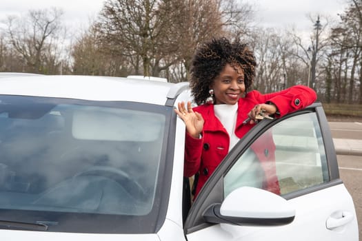 Confident african american businesswoman in red coat standing with white car