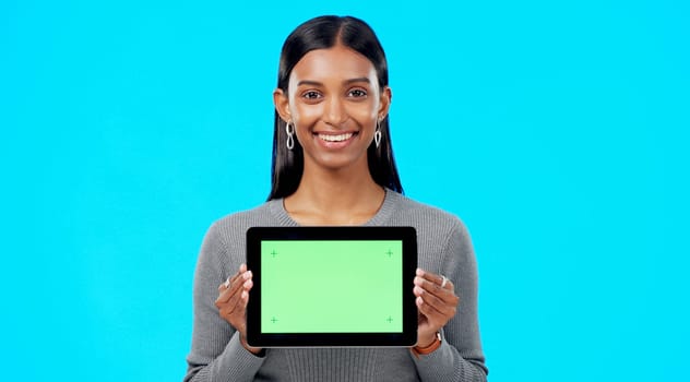 Mockup, green screen and face of a woman with a tablet isolated on a blue background in a studio. Branding, smile and portrait of an Indian girl holding technology with a blank screen for advertising