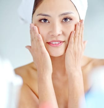 Silky smooth skin. An attactive young Asian woman applying moisturizer with a towel on her head.