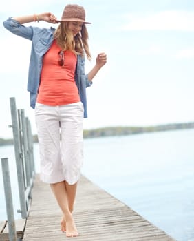 Happy to be on holiday. A happy young woman standing on a pier next to a lake.