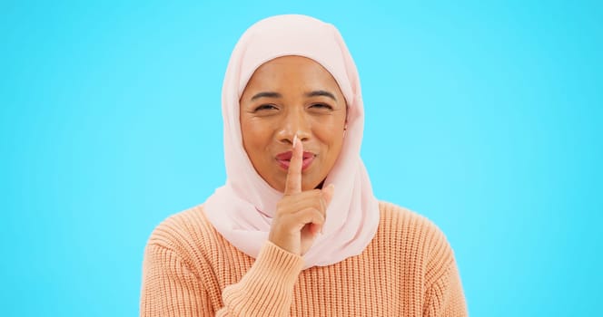 Muslim woman, finger on lips and secret with hand on mouth for mockup, advertising or promotion. Islamic female with hijab, face emoji or laugh for sale, gossip or surprise on studio blue background
