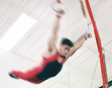 Gymnastics, ring and fitness with man in stadium and focus for sports, workout or health. Wellness, exercise and training with athlete and still rings in gym arena for strong, power and motion blur