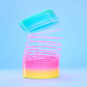 Rainbow slinky toy, spring and plastic product in studio isolated against a blue background mockup. Flexible toys, colorful spirals and childhood item stretched out for playing, having fun and games.