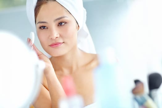 Maintaining her flawless beauty. An attactive young Asian woman applying moisturizer with a towel on her head.