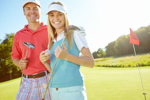 Tee time. Attractive young couple with their golf clubs and balls on the green.
