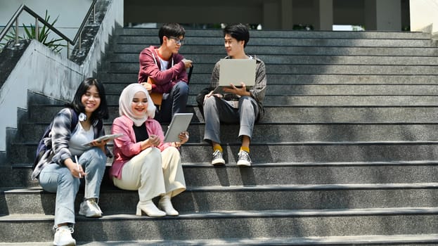 Group of students talking to each other after classes while sitting in front of university building