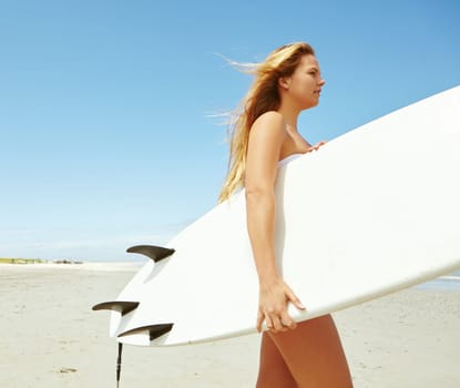 Surfing beauty. a young female surfer carrying her surfboard on the beach.