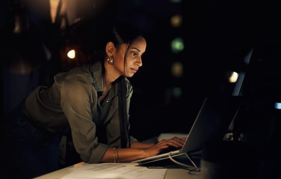 Keeping her mind on the deadline. a young businesswoman working on a laptop in an office at night.