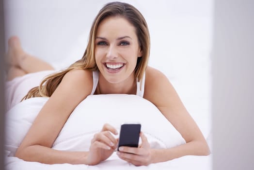 Texting in the morning...Portrait of an attractive young woman reading a text message on her bed.