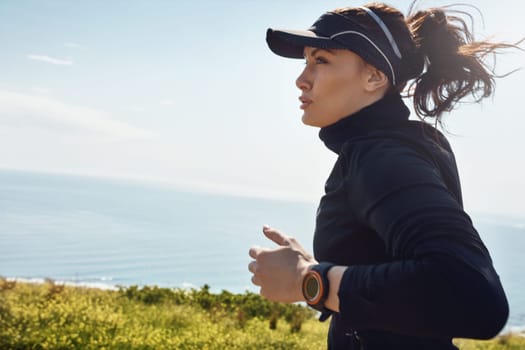 Her confidence and motivation goes hand in hand. a determined young woman going for a jog on her own with a view of the ocean in the background.