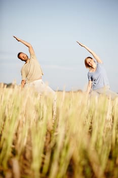 Stretch away the stress. a mature couple enjoying a yoga workout in a crop field.