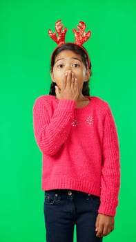Child, christmas and shocked on green screen for secret or sale studio background. Face of girl kid with antlers headband and hand on mouth for holiday celebration announcement, surprise or portrait