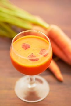 Carrot juice, vegetable and healthy food or drink with color, art and nutritionist creativity. Vegan smoothie or orange liquid in glass for wellness, diet or nutrition on a wooden table with ice.