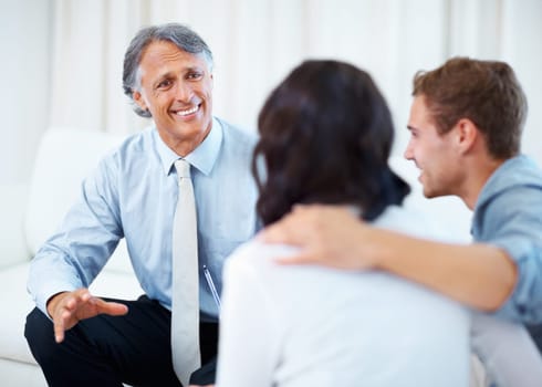 Financial planner discussing with young couple. Mature financial planner discussing with young couple at home.