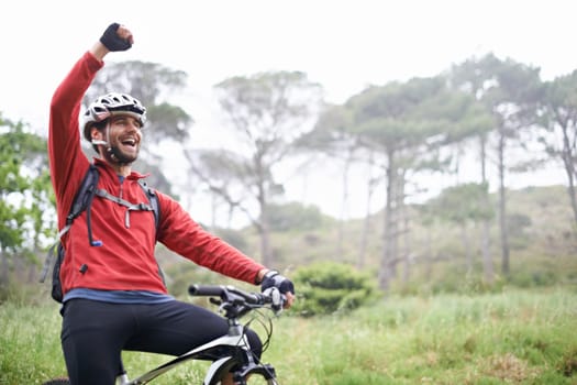 Pure exhilaration. A young male athlete pumping his fist in the air after conquering a mountain biking trail.