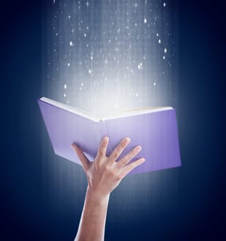Be drawn into new worlds. Shot of a hand holding an open storybook with light emanating from it.