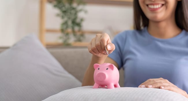Young smart Asian teenager putting coin in a piggy bank, happy young woman who puts coin in piggy bank for saving, investment economical
