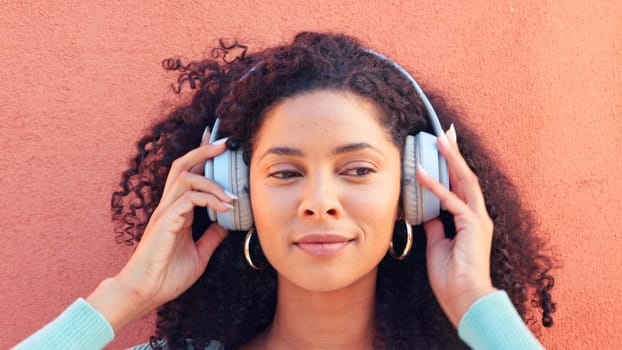 Music, headphones and face of a happy black woman listening to radio, song and sound against a wall background. African female head in wireless happiness, excitement and fun audio playlist outdoors