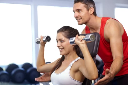 Sharing his expertise. A trainer helping a young woman with her weight-training at the gym.