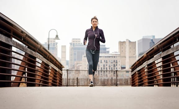 Fitness is a journey. Full length shot of an attractive young woman listening to music while running through the city