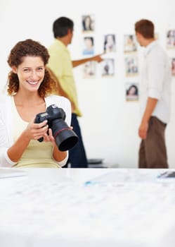 Smiling female photographer viewing images in camera. Portrait of smiling female photographer viewing images in camera with colleagues in background.