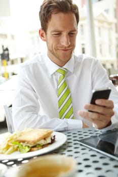 Meeting a friend for lunch. A young businessman sending a text message while sitting at an outdoor cafe.