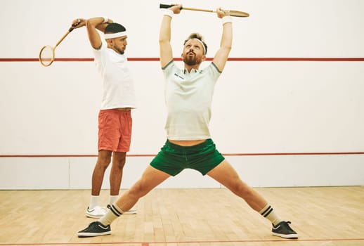 Reduce the risk of injury with a warmup. two young men stretching before playing a game of squash.