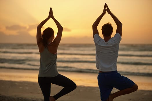 Exercise that invigorates body, mind and spirit. Rearview shot of a couple doing yoga on the beach at sunset.