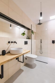 Loft style bathroom with toilet, big mirrors and sink and glass shower cabin with beige tile. The concept of renovation in a hotel or honeymoon room in a hostel. Copyspace